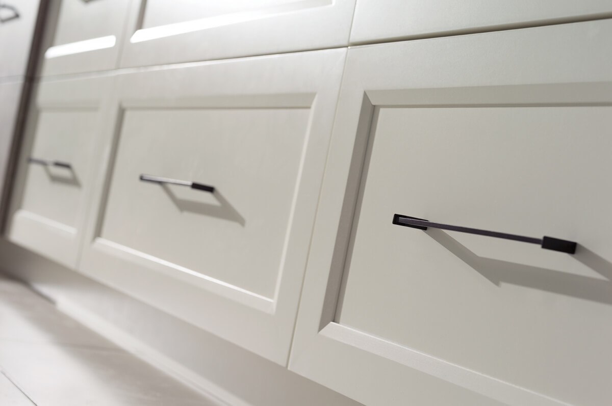A row of white painted flat panel drawer fronts in a transitional kitchen design. When considering cabinet construction methods, cabinetry is divided into two major categories — Framed and Frameless. What’s the difference between Framed and Frameless kitchen cabinetry? This modern kitchen shows full overlay cabinet doors on frameless construction.