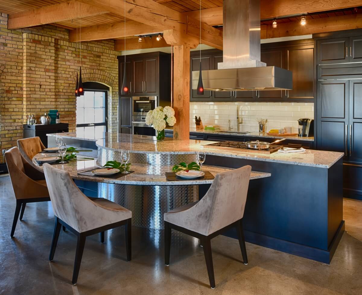 An Industrial Chic styled city loft with black painted cabinets and a curved kitchen island with table height seating and a large countertop overhang.