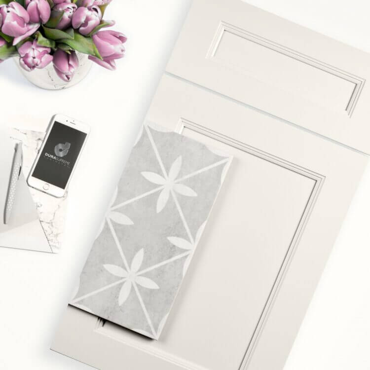 Dura Supreme's Meridien flat panel door style in the Linen White paint laying on a countertop with a gray and white backsplash tile.