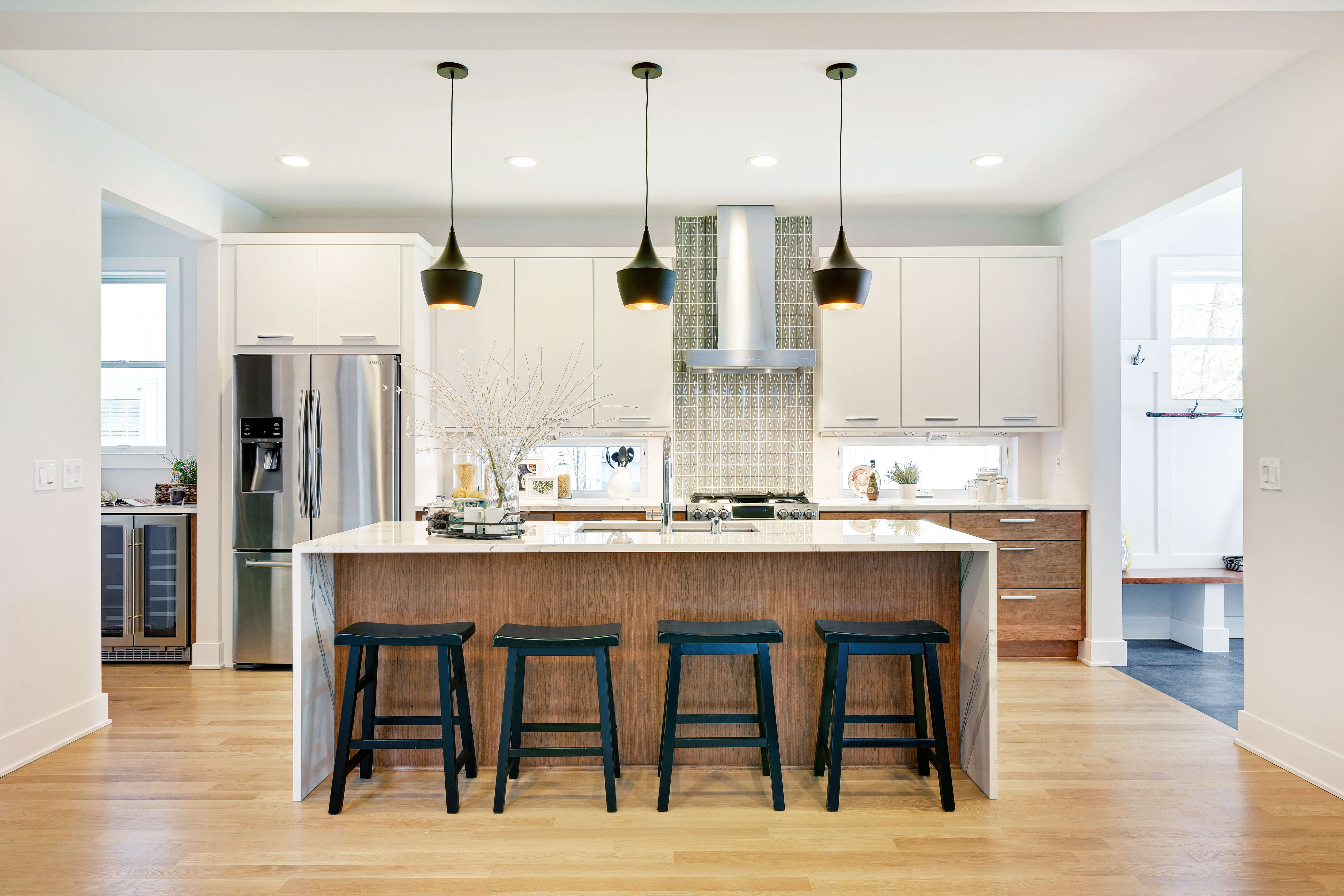 A contemporary kitchen with a sleek waterfall kitchen island. THe wall cabinets are painted white while the base cabinets and island are a stained wood color.