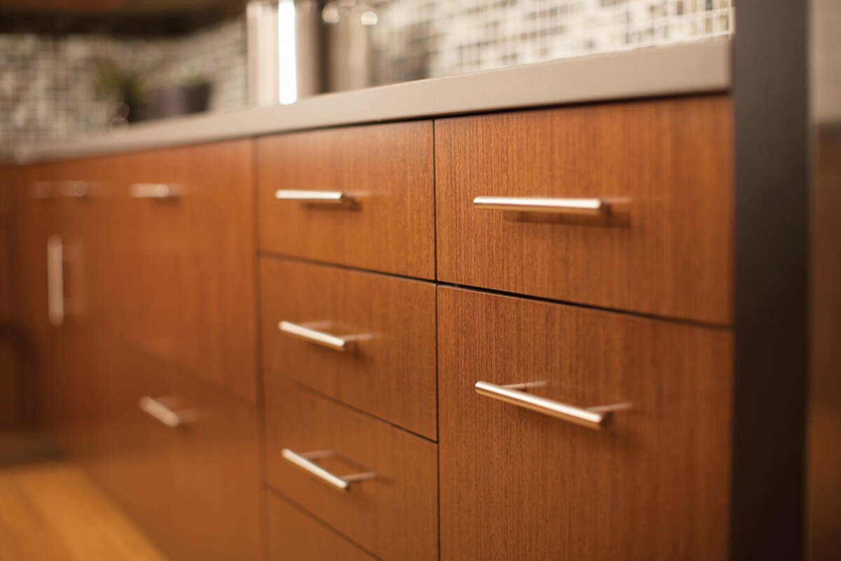 A row of slab door base cabinets in a contemporary kitchen with a rich, warm stain color with a reddish tint.