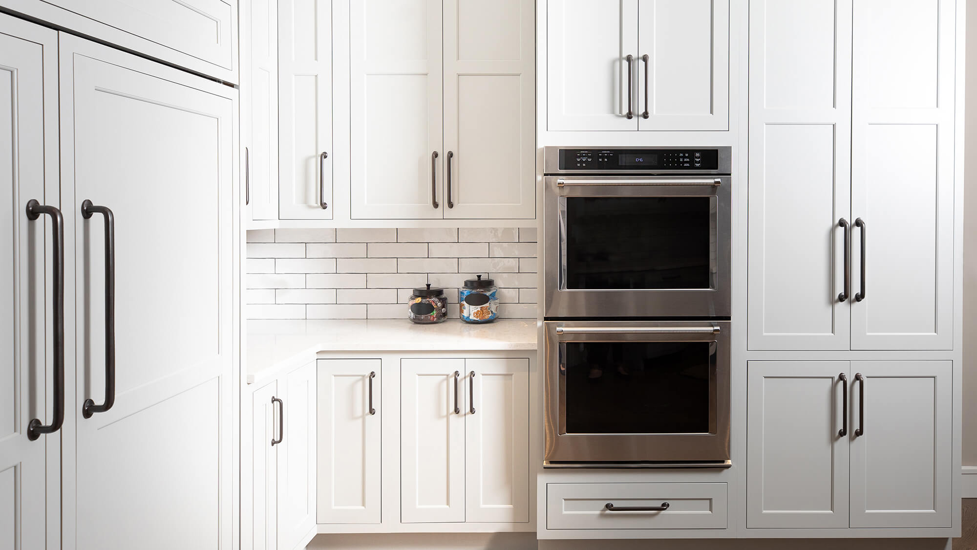 A well-designed appliance landing counter space next to two wall ovens and a paneled fridge.