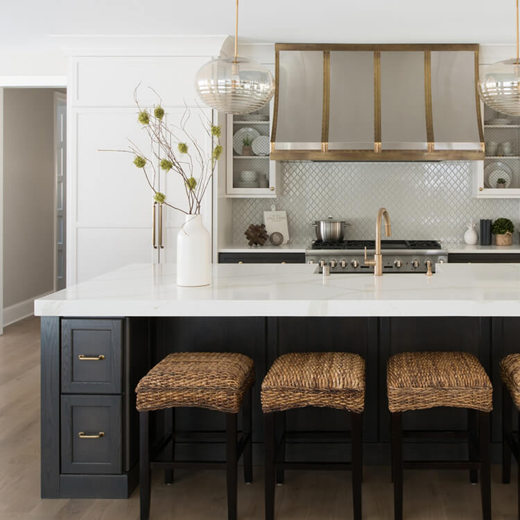 A stunning and trendy white and dark gray kitchen design with a dramatic gold hood over the cooking space.