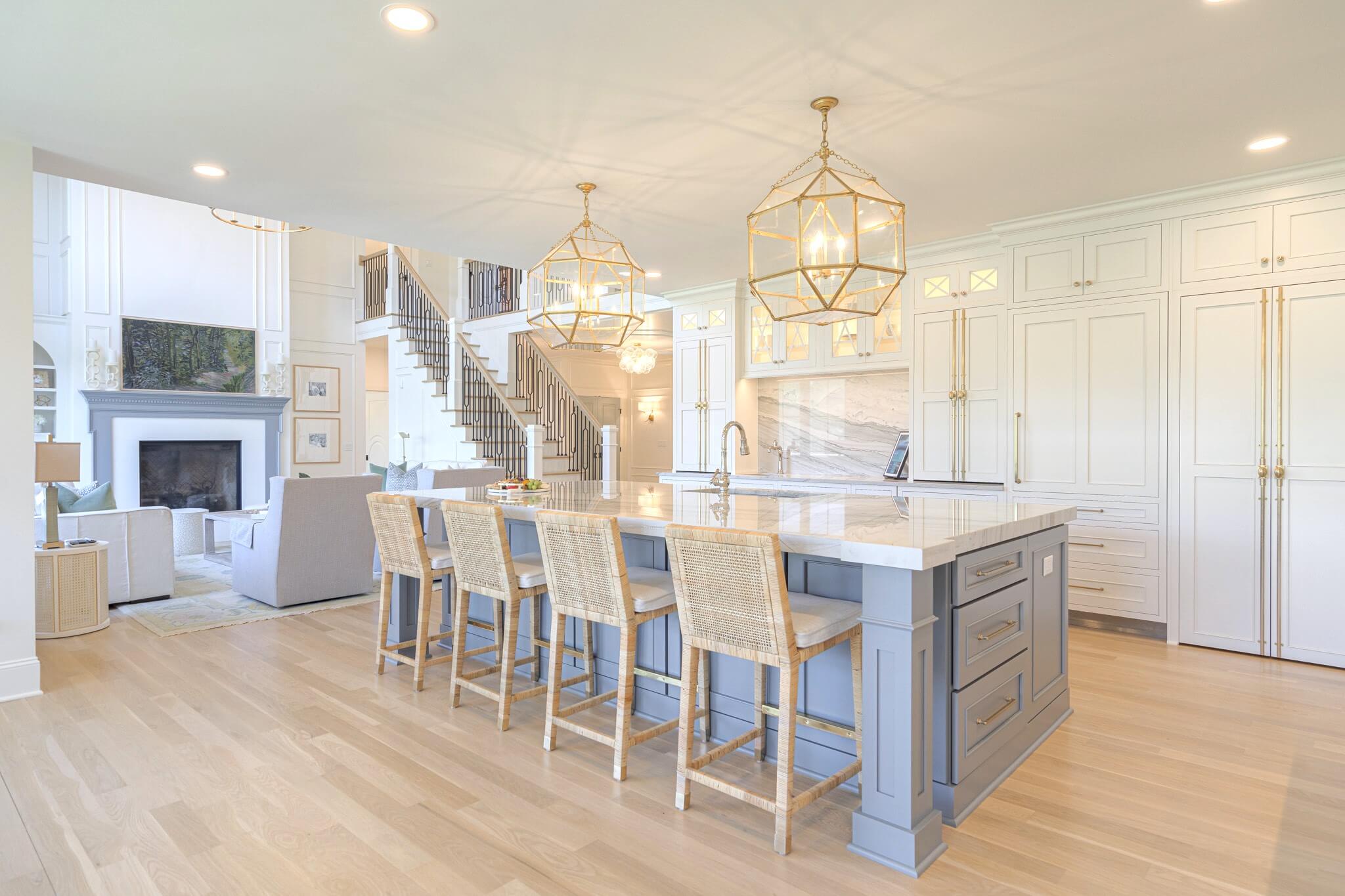 A beautiful white kitchen featuring a gray-blue painted kitchen island and fireplace mantel in the neighboring living room of this open-concept home.