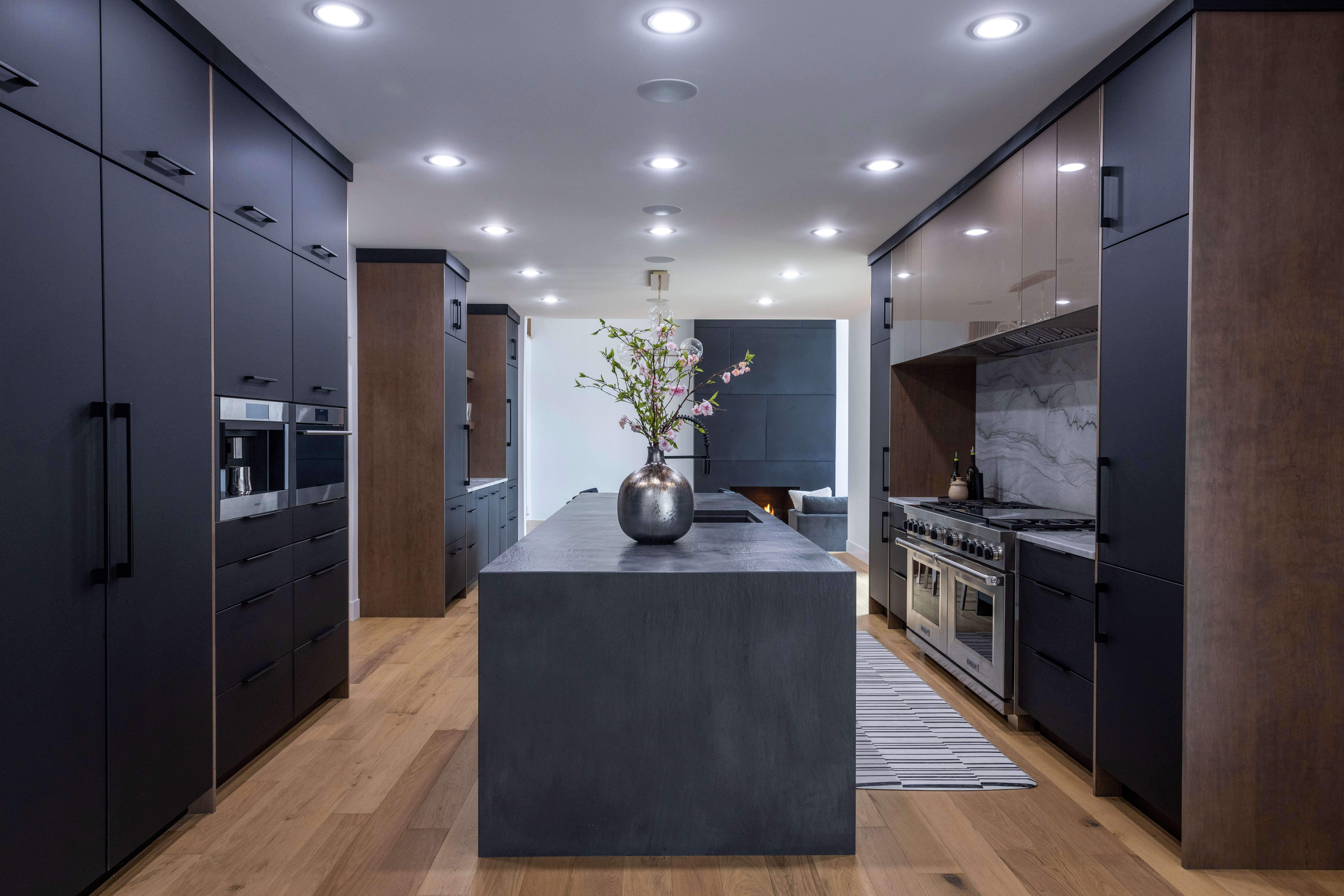 A dramatic, contemporary kitchen design with black and brown slab door cabinets and a sleek alcove range cooking zone space.