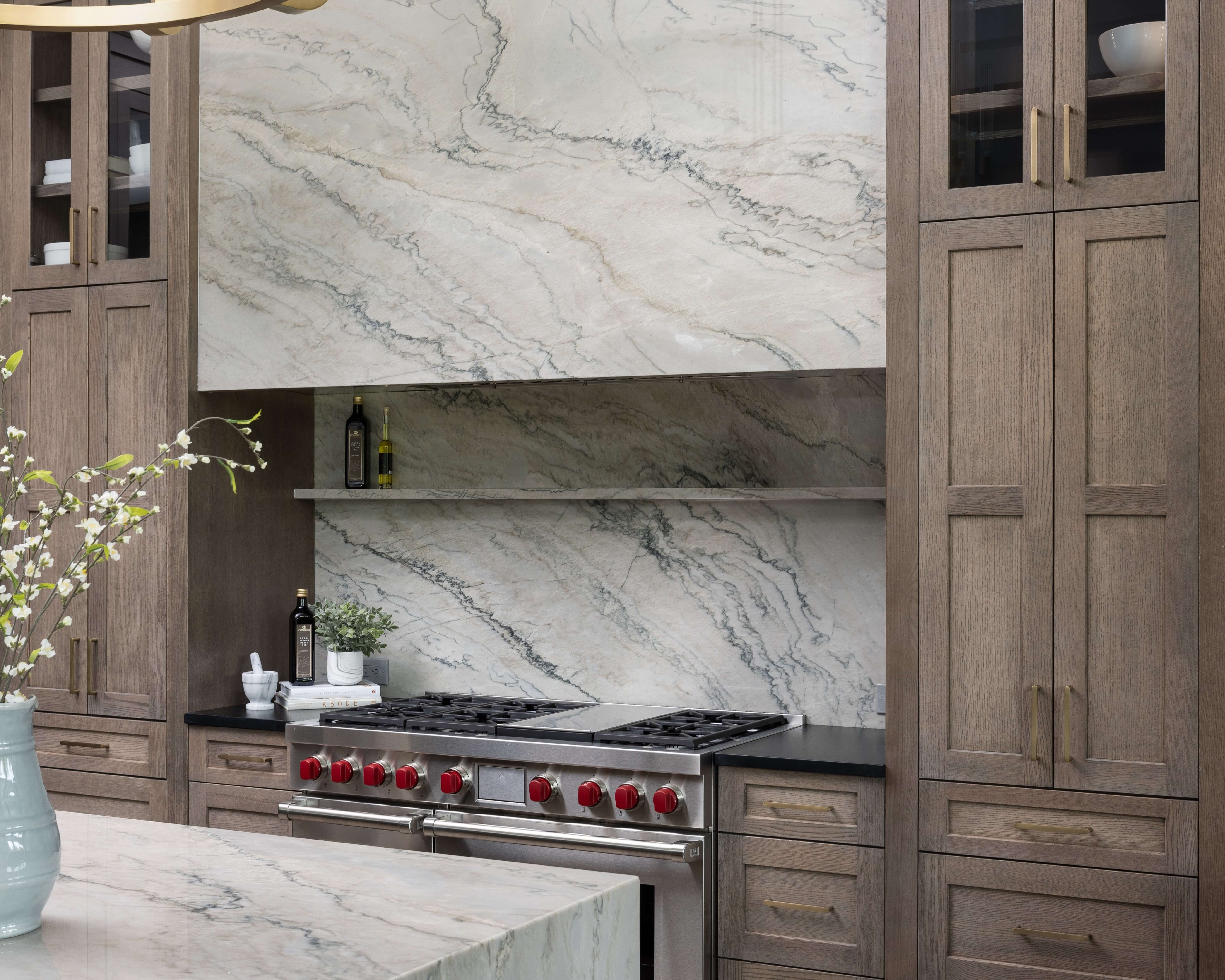 A stunning quartz hood, backspalsh, and floating shelf are surrounded with shaker wood cabinets to create a beautiful range alcove space.