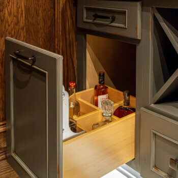A pull-out cabinet storage solution with a rack with dividers for bottle storage.