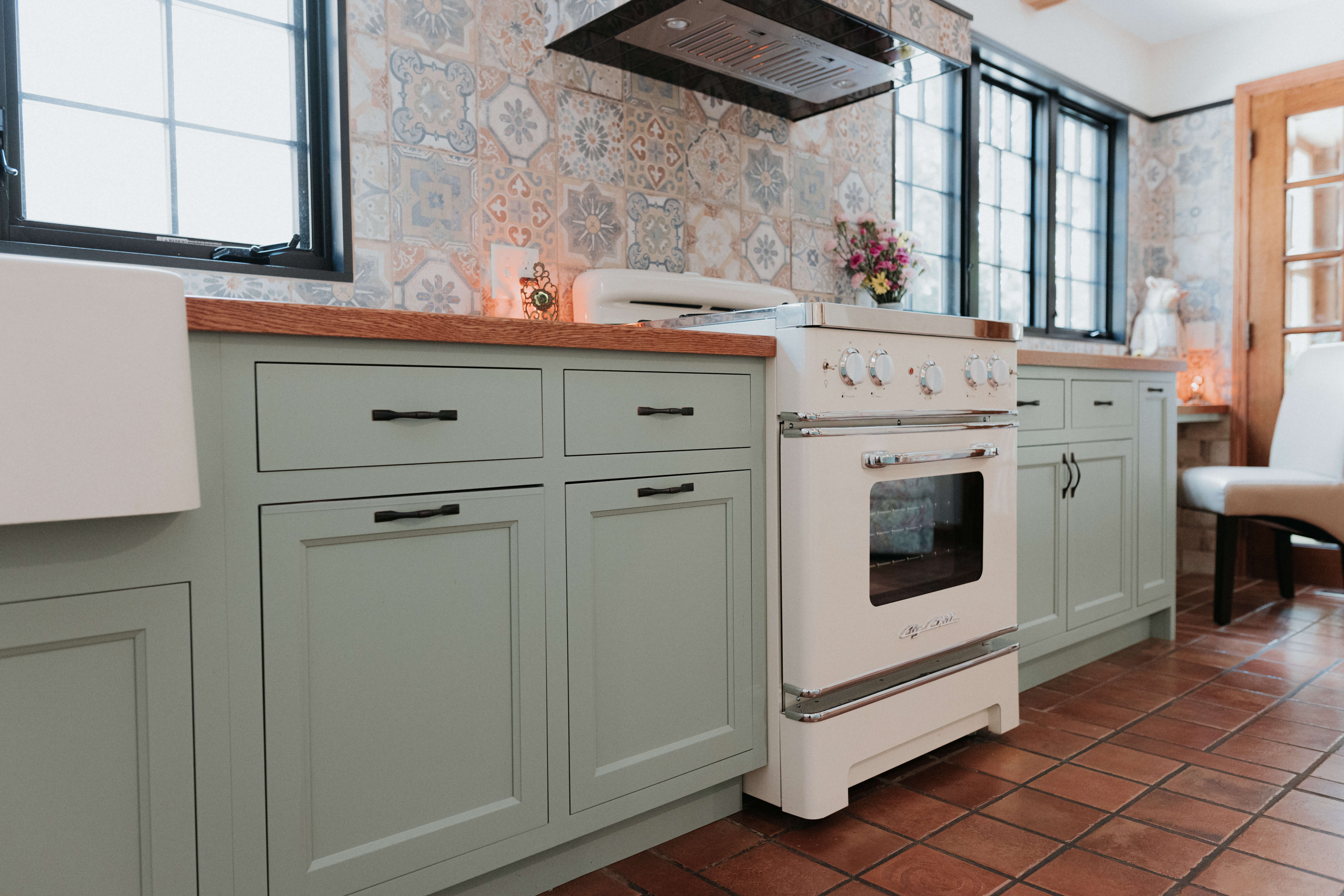 A bohemian kitchen with light green painted cabinets and a retro styled oven.