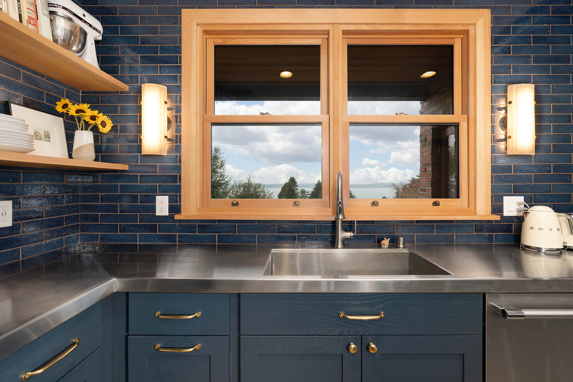 A navy blue color drenched kitchen design with a few light natural wood accents for contrast. The design combines glossy blue backsplash tiles with matte blue painted cabinets with a shaker door style.