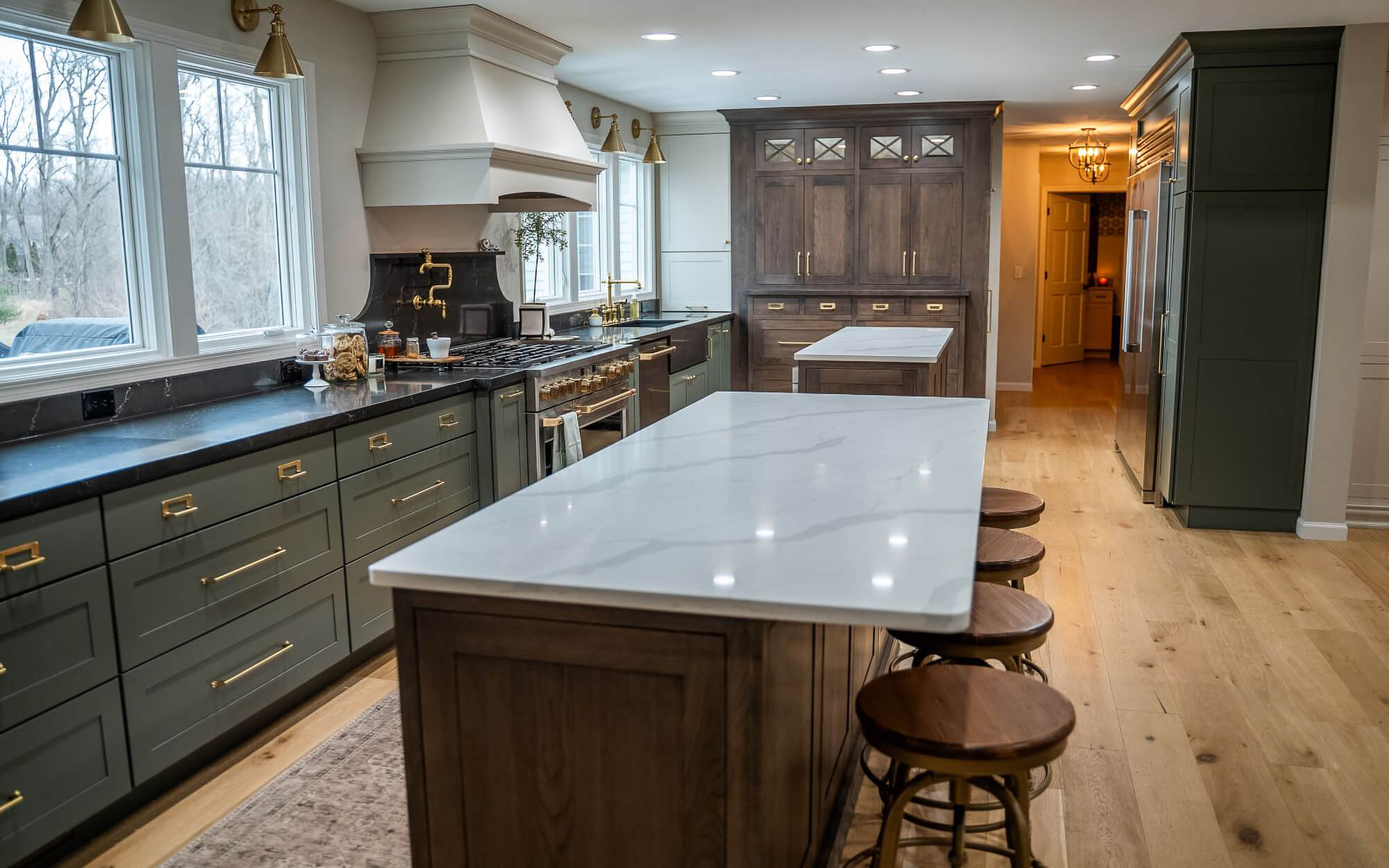 A long kitchen with two kitchen islands featuring green painted cabinets.