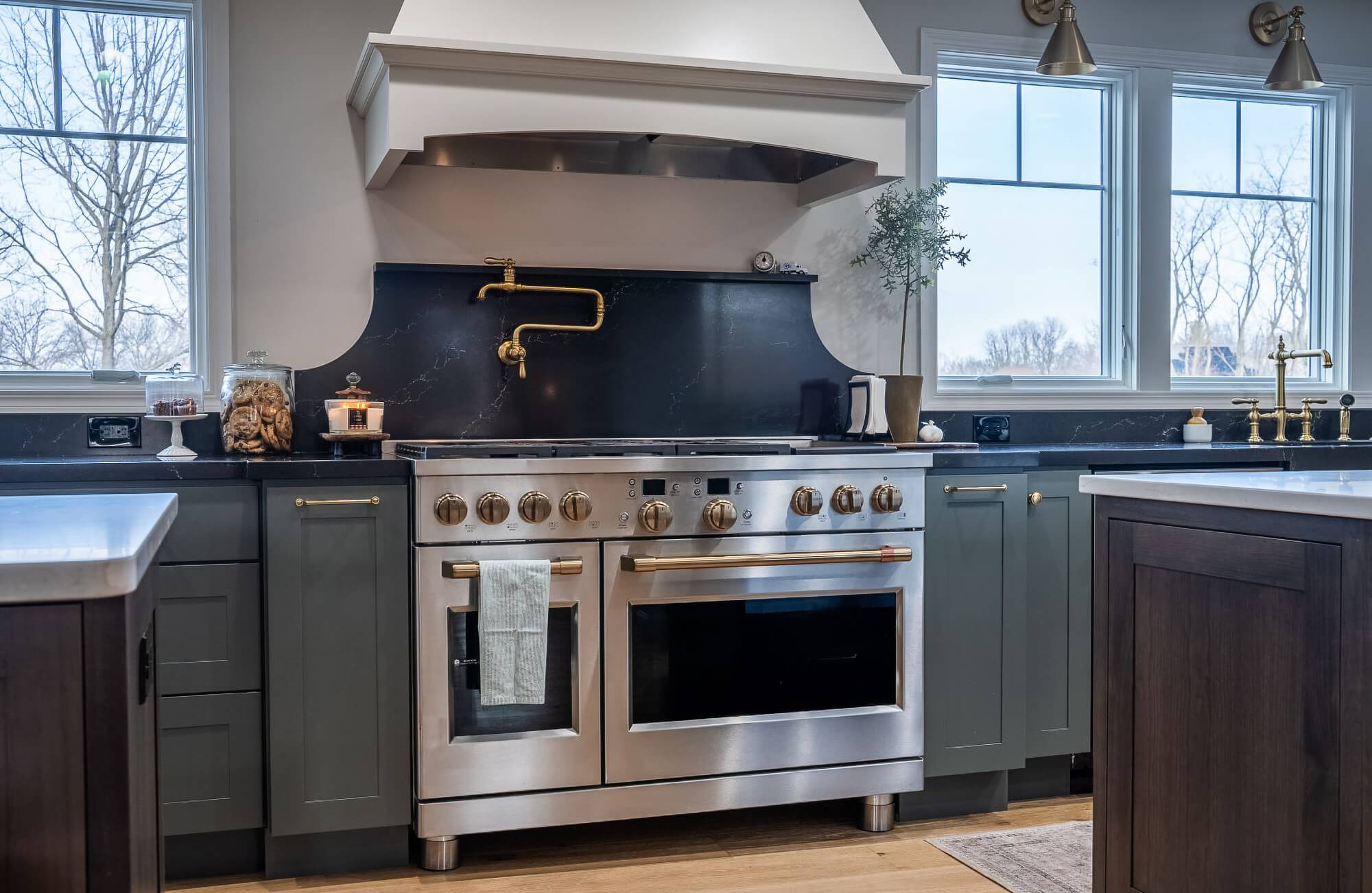 A green, white, and brown kitchen with an elegant cooking zone space with an independent wood hood and trendy green painted cabinets.