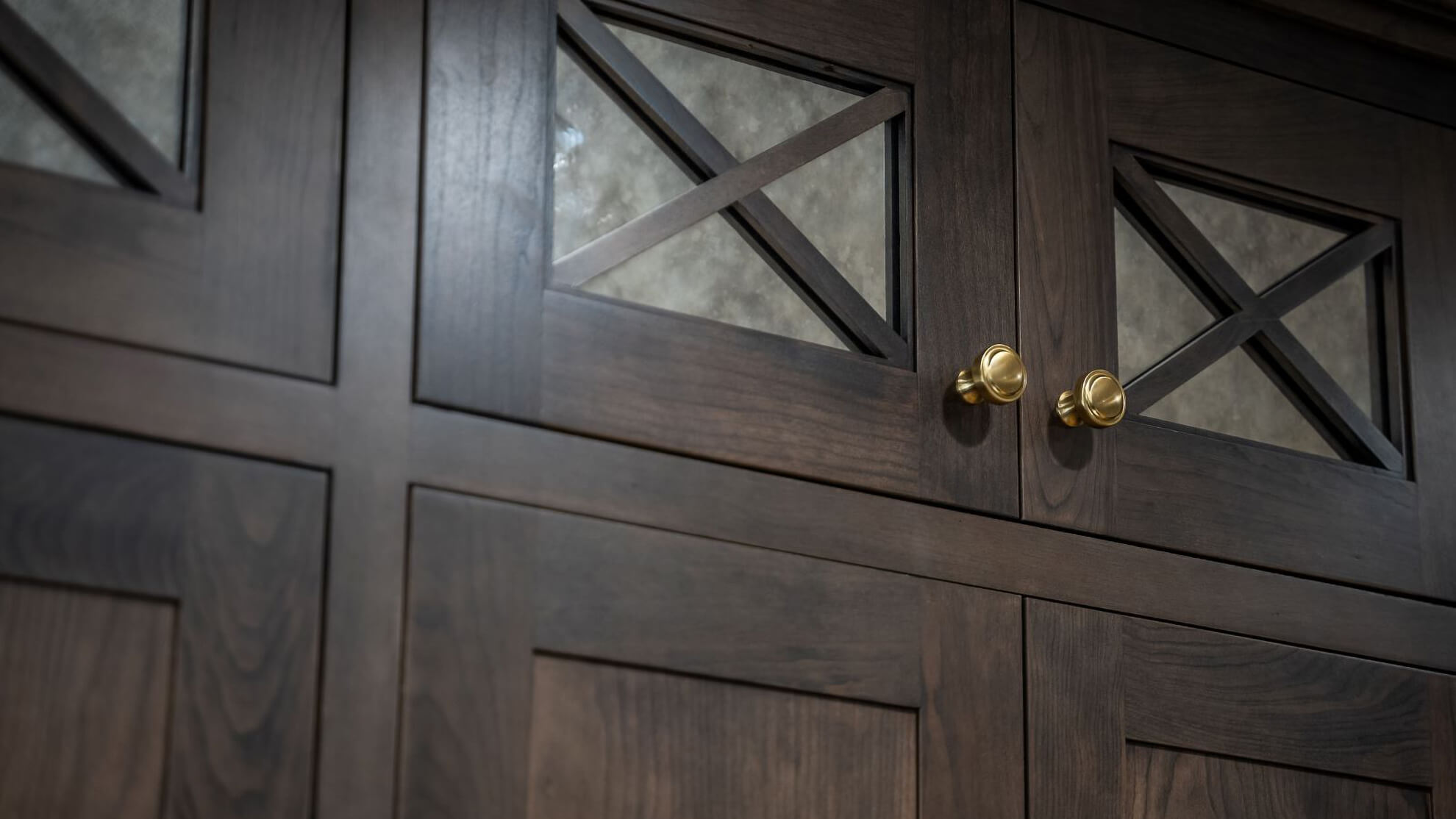 A close up of mullion cabinet doors with a rustic dark stained wood featuring antique mirror inserts for the cabinet doors.