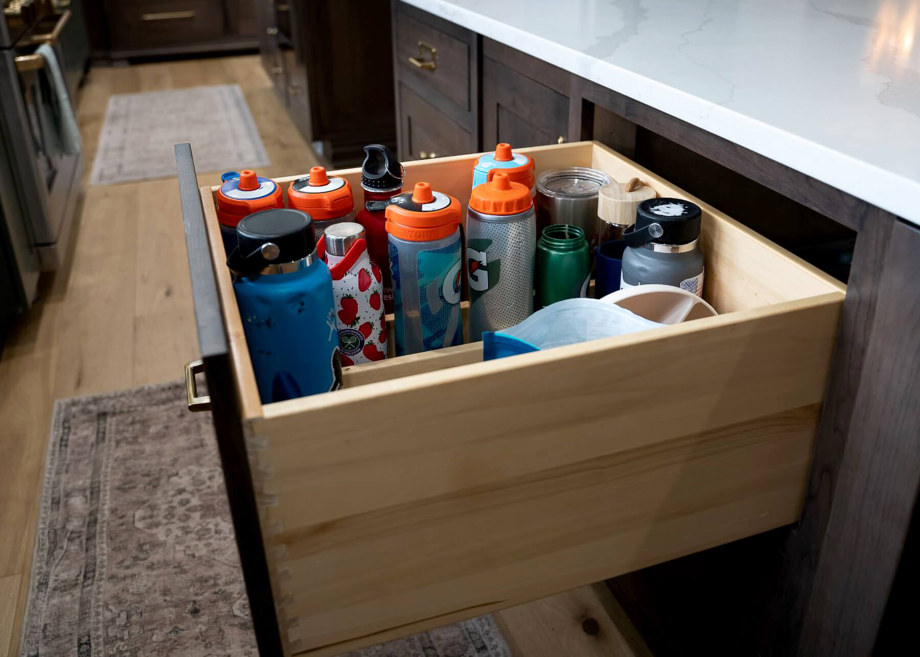 A deep drawer with organized storage for a collection of water bottles using drawer partitions.