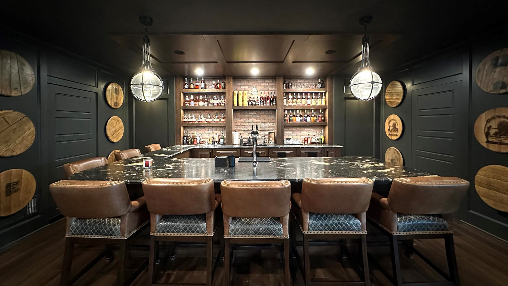 A moody home bar design with a dark, rustic wood and black painted walls.