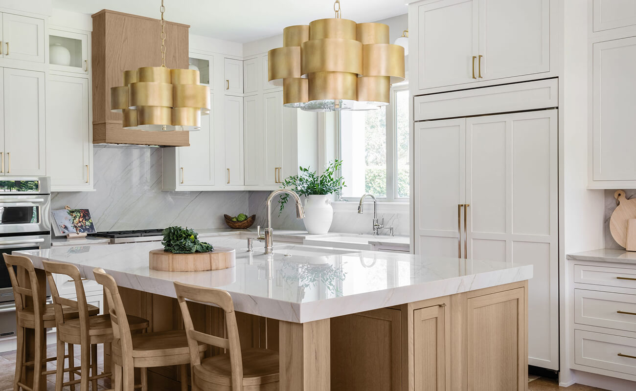 A beautiful kitchen with white painted cabinets with contrasting light stained wood hood and kitchen island.