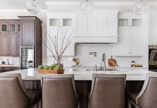 A transitional and casual kitchen design with elegant finishes. A grand white painted wood hood takes center stage over the knotty alder kitchen island.