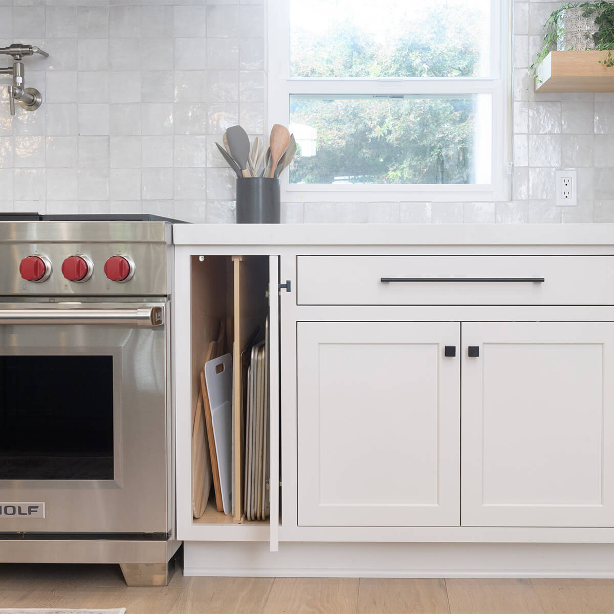A thin cabinet next to the oven has a vertical partition to divide the storage for pans, baking sheets, and muffin tins.