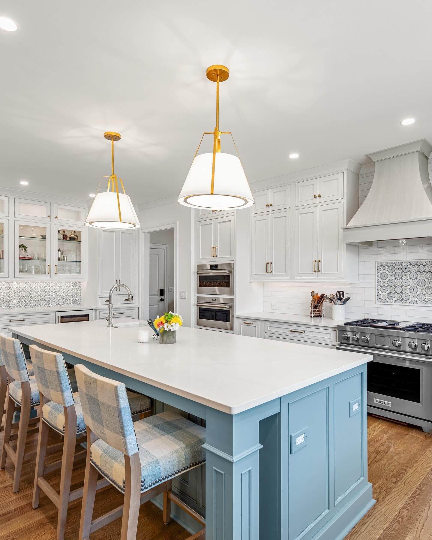 A gray and white traditional styled kitchen with classic inset cabinet doors featuring a gray kitchen island surrounded by white painted inset cabinets and curved wood hood.